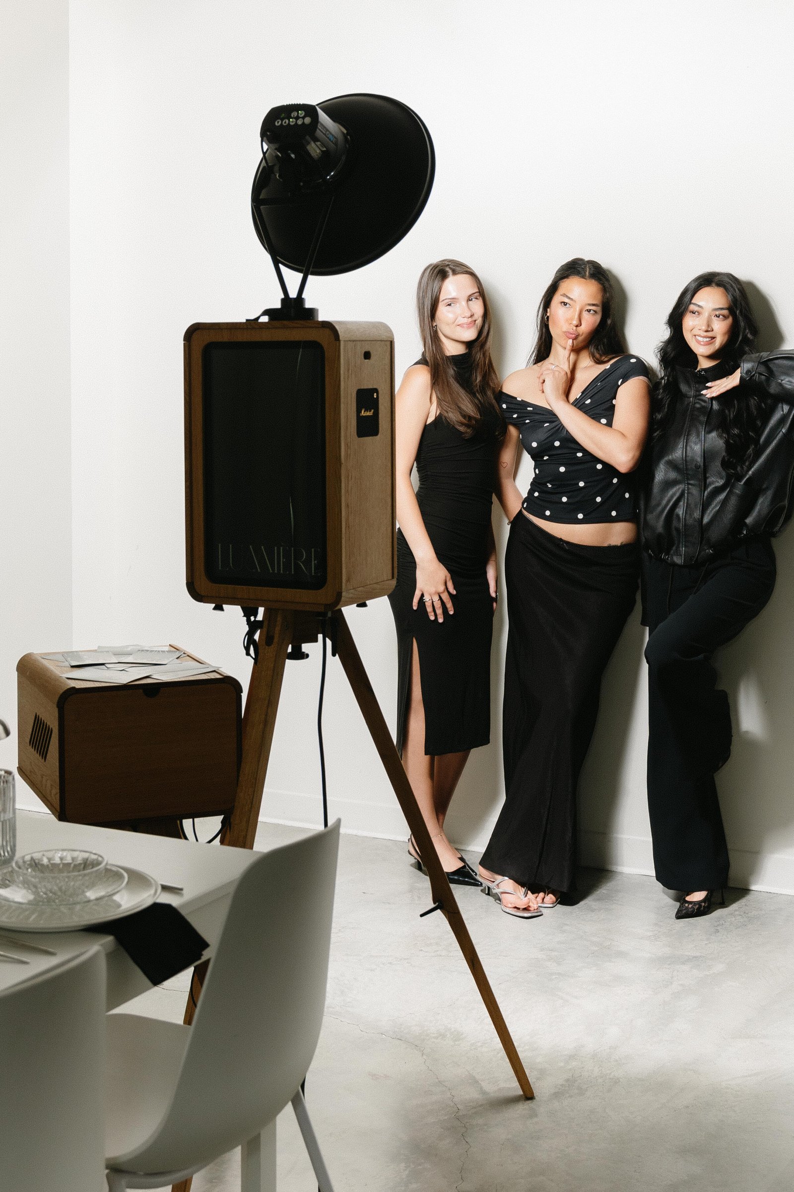 Three guests posing beside the open-air photo booth and its softbox light