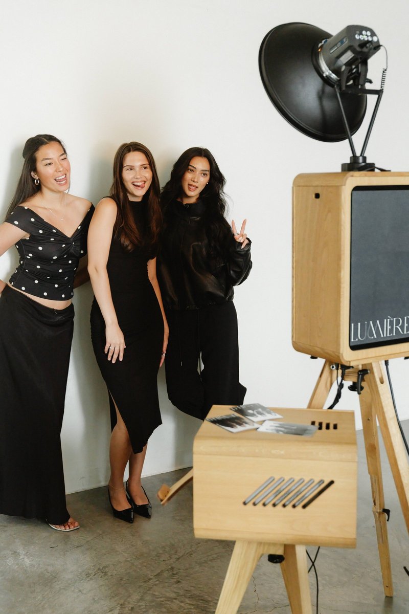 Three guests in black posing next to the open-air photo booth on its wooden stand