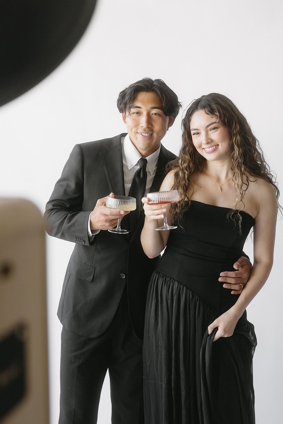 A couple in formal wear toasting with cocktails in a studio portrait