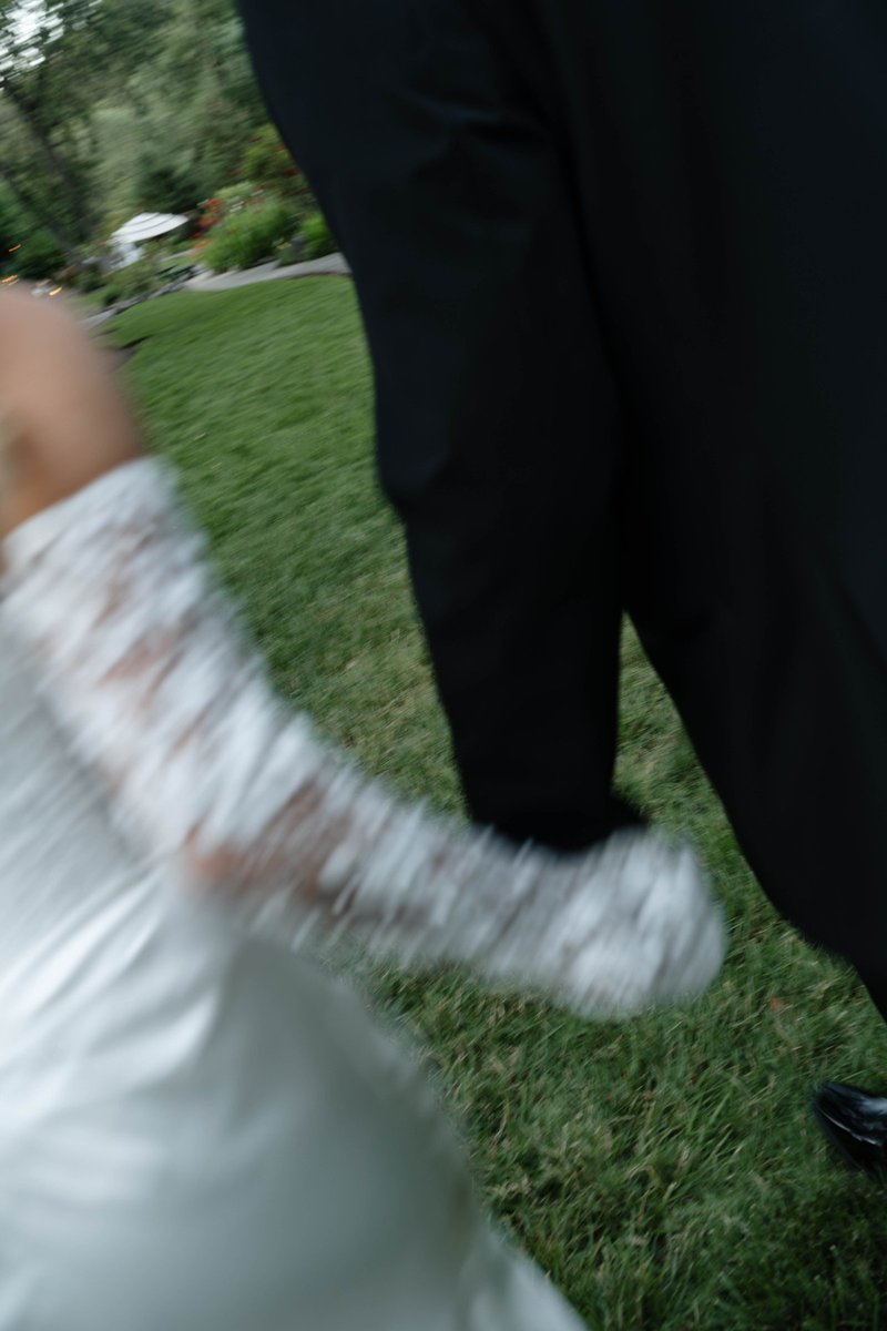 A bride's lace-gloved hand holding her partner's hand as they walk across the lawn