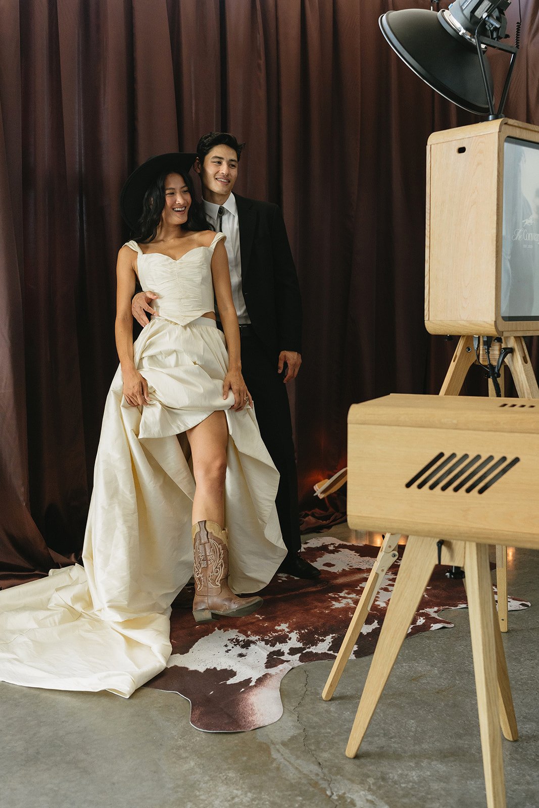 A bride lifting her gown beside the open-air photo booth on its wooden tripod