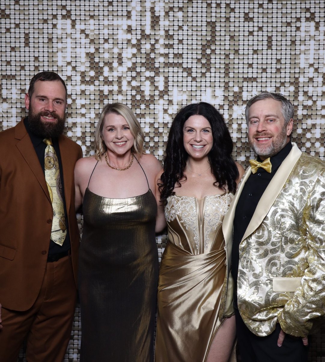 Four colleagues in black tie against a gold sequin backdrop