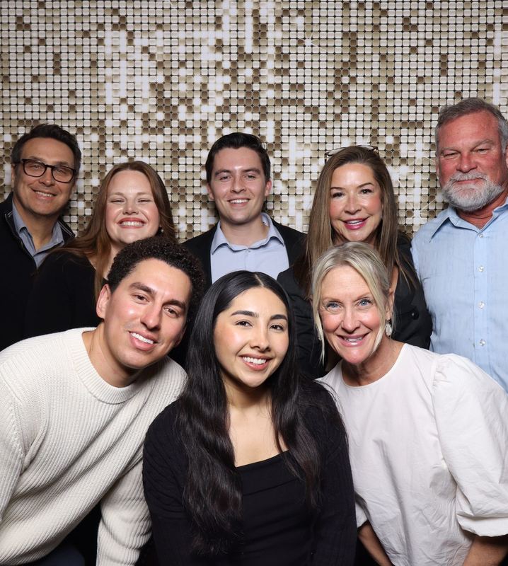 A group of coworkers smiling in front of a gold sequin backdrop