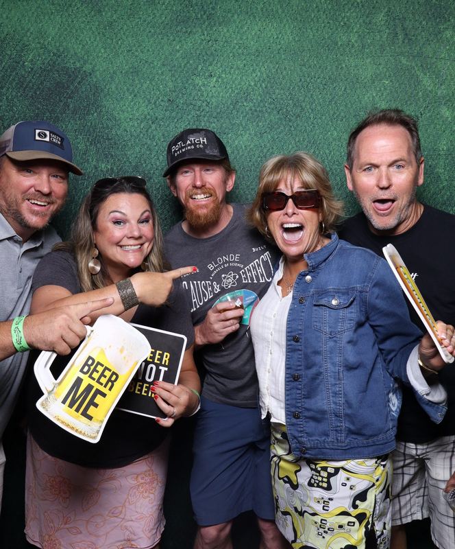 Coworkers laughing with a Beer Me sign in front of a green backdrop