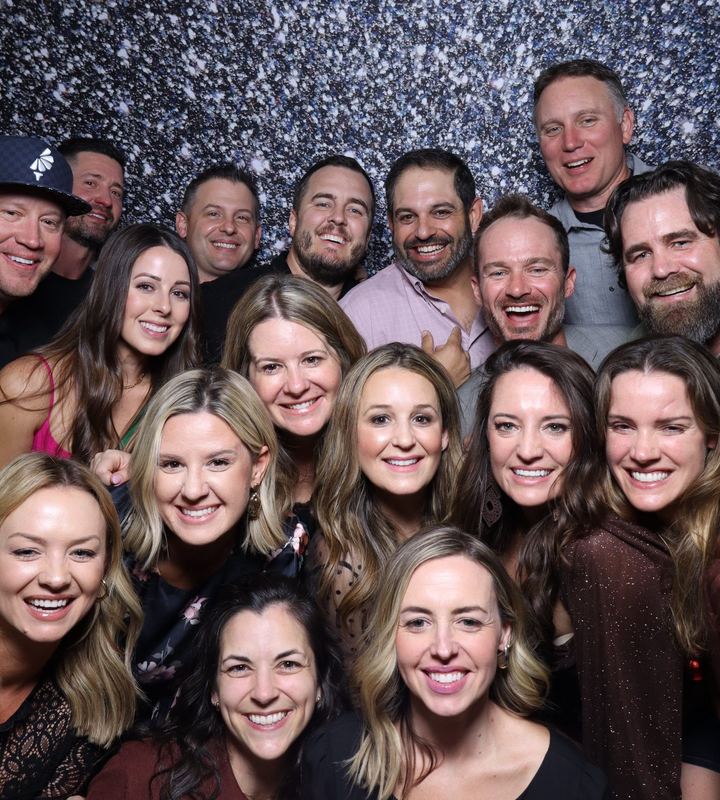 A large group crowded together in front of a silver sequin backdrop