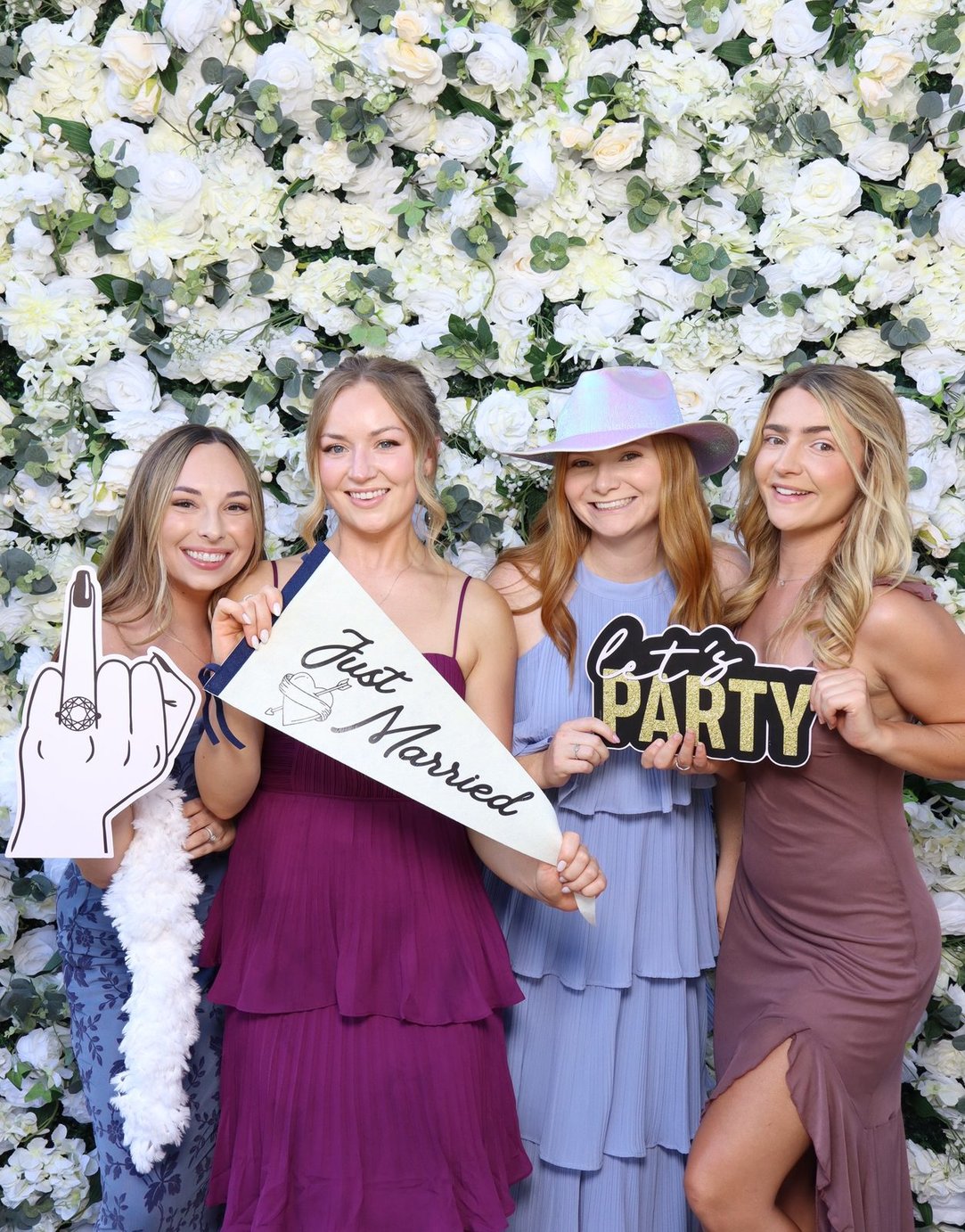 Bridesmaids with just married props at the flower wall