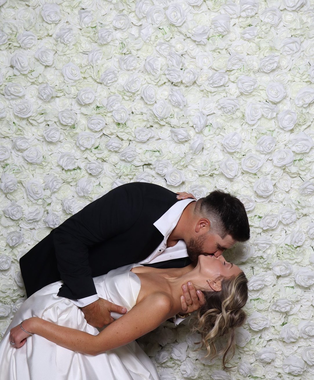 A groom dipping the bride in front of the flower wall