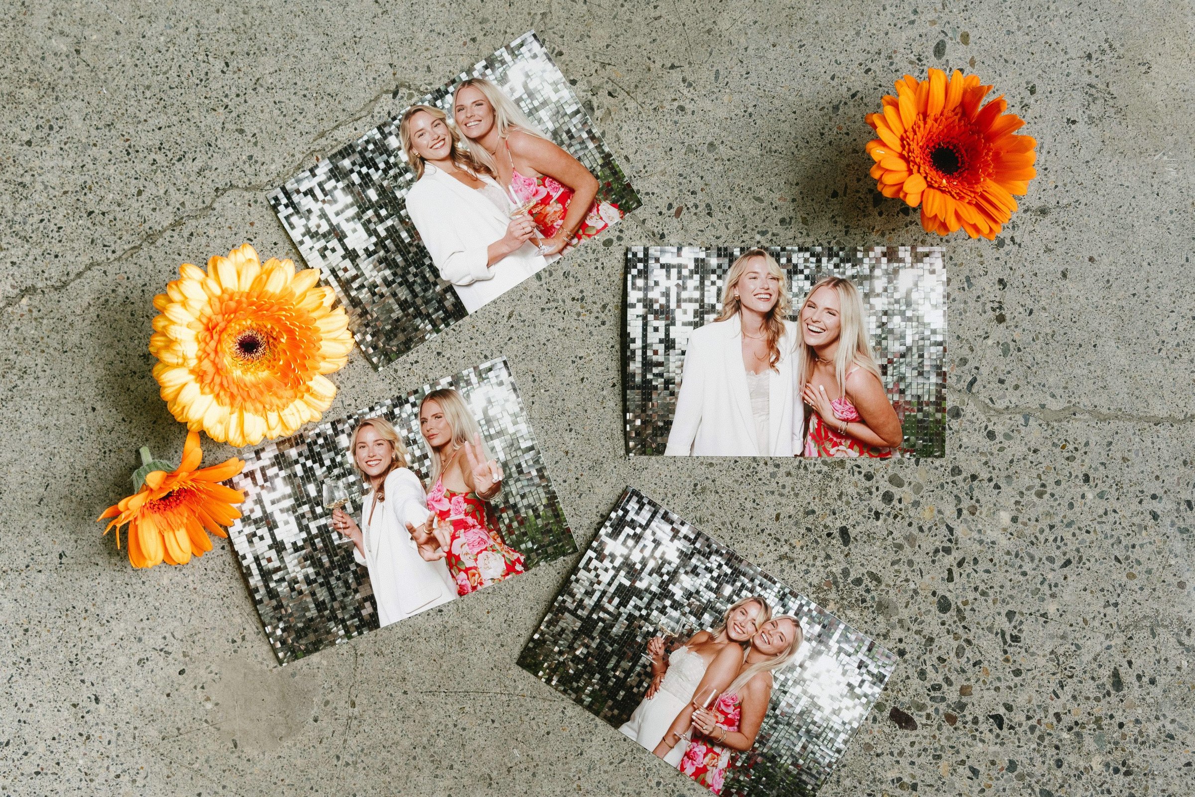 Photo booth prints scattered on concrete with orange gerbera daisies