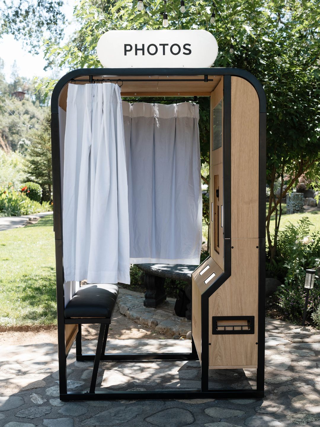 The Classic Vintage Enclosed booth with white curtains and a PHOTOS sign set up outdoors